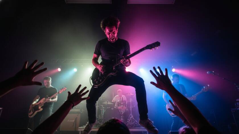 A dynamic, wide-angle shot of a lead guitarist mid-shred under dramatic purple and blue stage lights at a vibrant Delahey live music venue, perfectly encapsulating Delahey concert photography capturing electrifying live music in Melbourne's north-west. The crowd's hands are visible in the foreground, blurred with motion, adding to the intense atmosphere.
