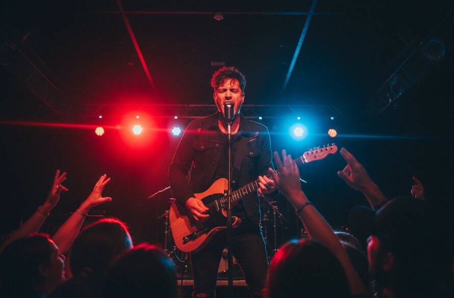 Dramatic shot of a lead guitarist mid-shred at a Donvale live music photography unforgettable moments event, stage lights creating a halo effect, crowd hands raised in enthusiasm, capturing raw energy and passion.