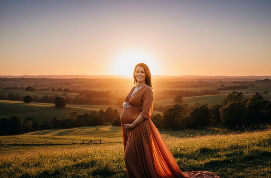 A pregnant woman in an elegant flowing gown, silhouetted against a dramatic Drouin sunset, showcasing Drouin maternity photography capturing your radiant journey, with golden light illuminating her silhouette and the rolling hills of Gippsland in the background.