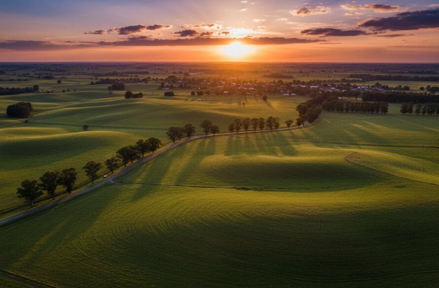 An awe-inspiring aerial photograph showcasing Drouin Victoria drone photography breathtaking landscapes, capturing a dramatic sunset over rolling green hills and distant mountain ranges, with a winding country road leading towards the horizon, professionally colour-graded for a cinematic feel.