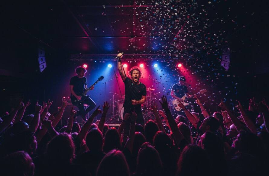 A wide shot of a band performing on stage at a bustling local venue in The Basin, Victoria, capturing the dynamic concert photography The Basin spirit, with vibrant stage lights silhouetting the lead singer mid-song, confetti in the air, and an energetic crowd with hands raised, perfectly illustrating an epic moment.