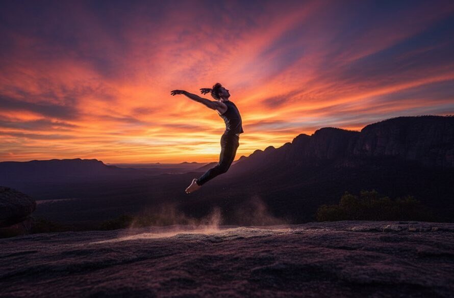 A male dancer in mid-air, silhouetted against a dramatic sunset over the Grampians near Ararat, performing an acrobatic leap, showcasing dynamic dance photography Ararat performance with professional lighting.
