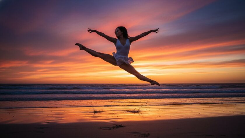A female contemporary dancer in an exquisite, dynamic pose on the iconic Ninety Mile Beach at sunset in Lakes Entrance, Victoria. Her movement is captured mid-air, silhouetted against a dramatic orange and purple sky, with the waves crashing gently in the background. Professional color grading enhances the cinematic mood. This epic moment showcases the artistic beauty of dynamic dance photography sessions Lakes Entrance.