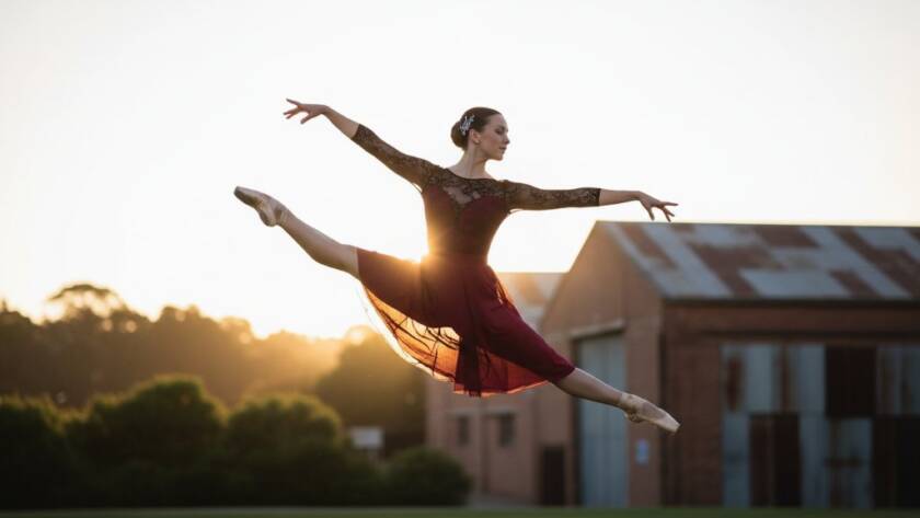 A dancer in a dramatic, athletic pose mid-air, bathed in golden hour light, performing against a blurred industrial Eumemmerring backdrop, showcasing the power of dynamic dance portraits Eumemmerring Victoria.