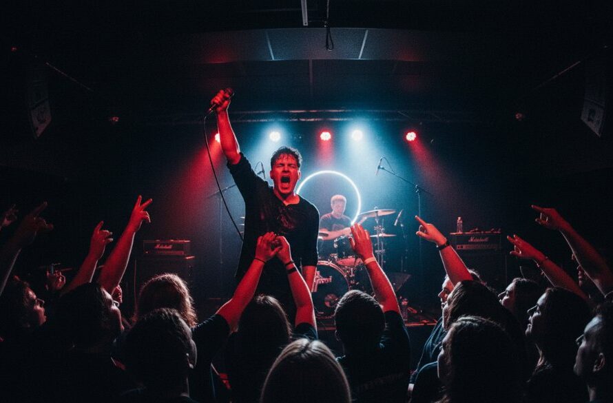 Dramatic wide shot capturing the raw energy of a band performing on stage in a packed Geelong venue, with vibrant stage lights silhouetting the lead singer and a crowd with hands raised, exemplifying dynamic Geelong live music photography.