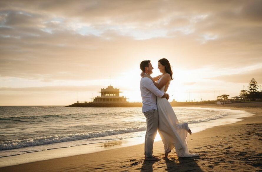 A candid, romantic, and beautifully lit 'epic moment' photograph of a couple embracing at one of the best East Geelong pre-wedding photoshoot locations, with the iconic Eastern Beach promenade and its art deco bathing pavilion visible in the soft golden hour glow, capturing their joyful anticipation.