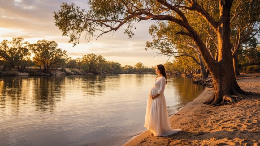 A breathtaking, professional photograph capturing an expectant mother's radiant silhouette at sunset along the Murray River during an Echuca Murray River maternity photography experience, with dramatic golden light filtering through ancient river gums, conveying serenity and anticipation.