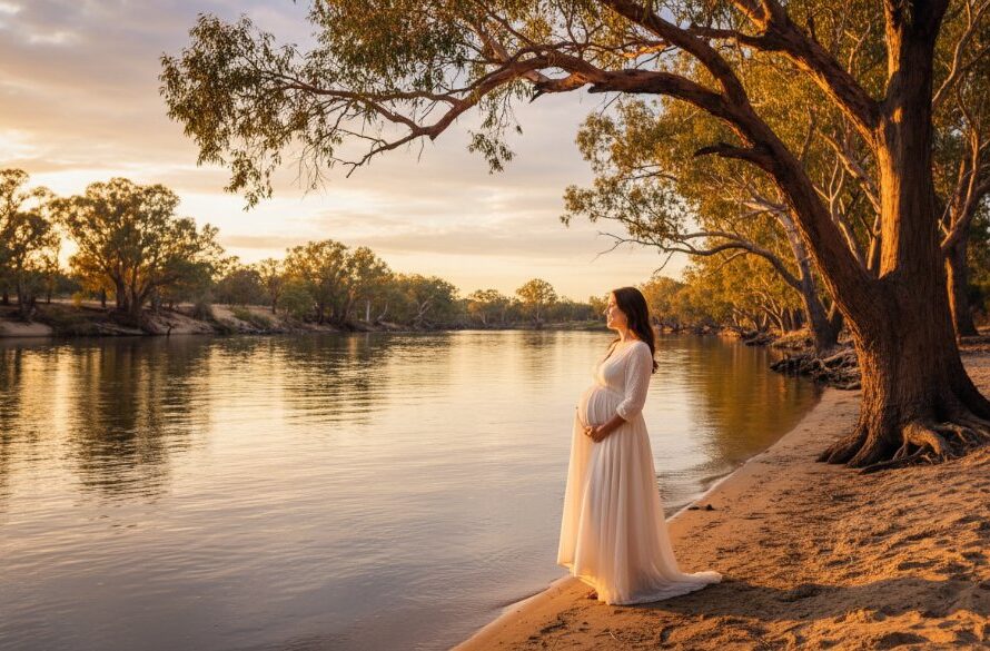 A breathtaking, professional photograph capturing an expectant mother's radiant silhouette at sunset along the Murray River during an Echuca Murray River maternity photography experience, with dramatic golden light filtering through ancient river gums, conveying serenity and anticipation.