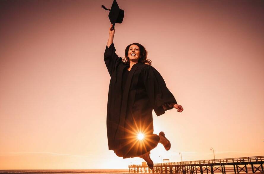 A jubilant graduate, cap thrown high, silhouetted against a golden sunset on Edithvale beach, celebrating their academic achievement. This epic moment for Edithvale beach graduation portraits Melbourne perfectly captures joy and triumph.