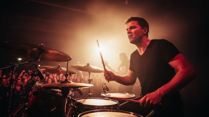 Dynamic wide-angle shot capturing electrifying Noble Park concert photography moments of a lead guitarist mid-solo on stage, bathed in vibrant blue and purple stage lights, with a cheering crowd silhouetted in the foreground, showcasing intense energy and a professional aesthetic.