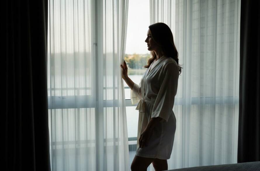 A stunning black and white portrait capturing an intimate, powerful moment of a woman during an elegant boudoir photography Sanctuary Lakes empowering women session, with dramatic light streaming through a window.