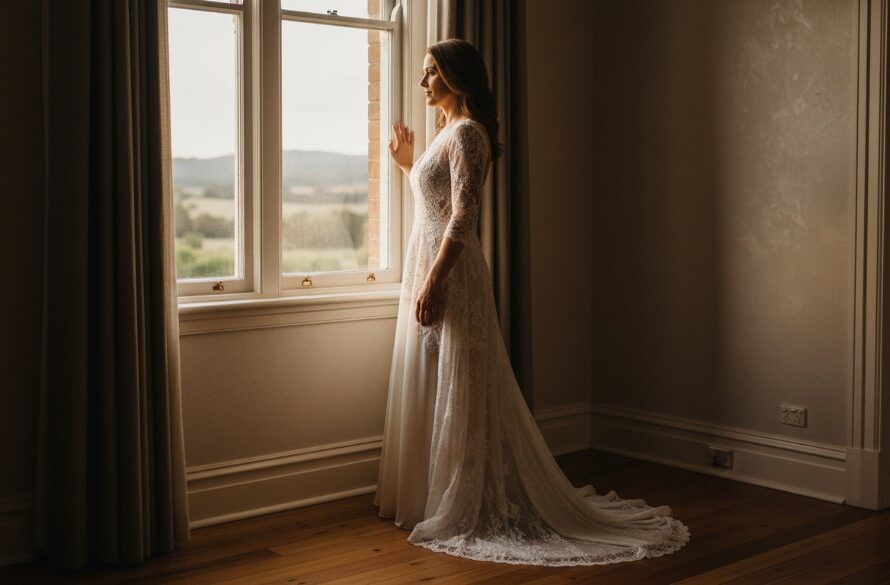 A beautifully composed, dramatic photograph of a woman bathed in soft, ethereal light by a window, capturing an empowering boudoir photography Stawell moment of serene confidence and intimate reflection. The image features professional depth of field and warm, cinematic colour grading, evoking timeless elegance.