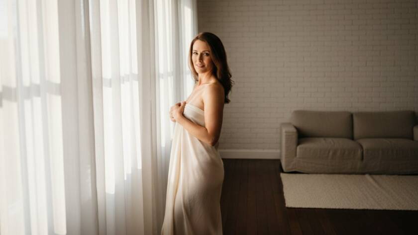 A dramatic, professionally lit photograph of a woman exuding confidence during her Empowering Boudoir Photoshoot Lang Lang Studio session, bathed in soft, ethereal light near a large window, capturing a powerful moment of self-discovery and inner strength.
