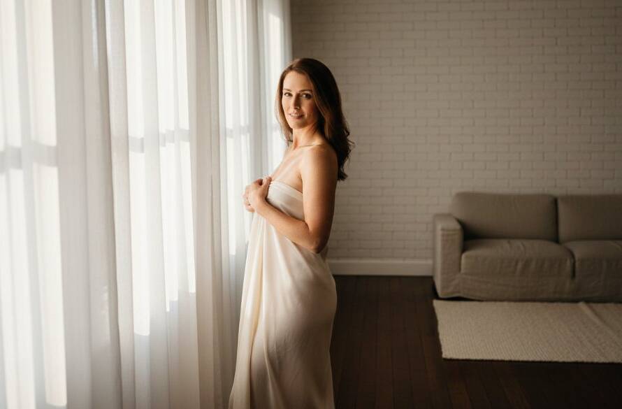 A dramatic, professionally lit photograph of a woman exuding confidence during her Empowering Boudoir Photoshoot Lang Lang Studio session, bathed in soft, ethereal light near a large window, capturing a powerful moment of self-discovery and inner strength.