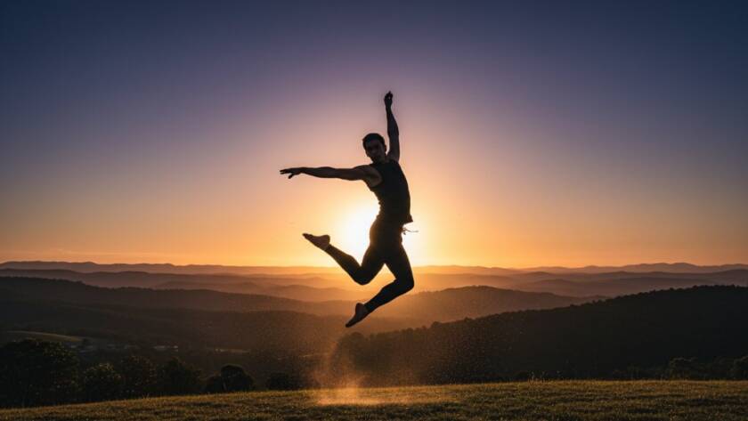 An epic moment of energetic dance photography in The Basin, showcasing a dancer mid-air, silhouetted against a golden hour sunset over the Dandenong Ranges, with dramatic backlighting highlighting powerful movement and emotion.