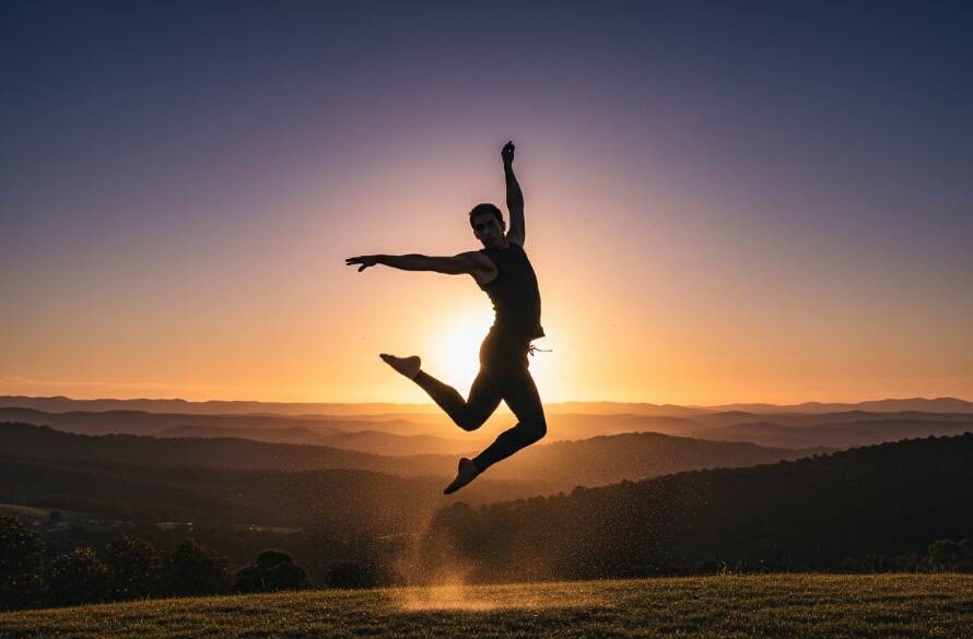 An epic moment of energetic dance photography in The Basin, showcasing a dancer mid-air, silhouetted against a golden hour sunset over the Dandenong Ranges, with dramatic backlighting highlighting powerful movement and emotion.