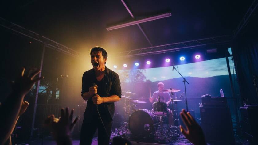 A wide-angle shot capturing an epic live concert photography Upper Ferntree Gully Victoria moment: A lead guitarist mid-shred under dramatic spotlights, sweat flying, audience hands raised, bathed in vibrant blue and red stage lights, conveying raw energy and passion.