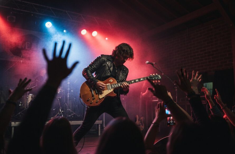 A dynamic, wide-angle, low-light photograph capturing an epic live music moment at a Sale Victoria photography concert, featuring a lead guitarist mid-shred with dramatic stage lighting, crowd hands raised in the foreground, and a vibrant energy.