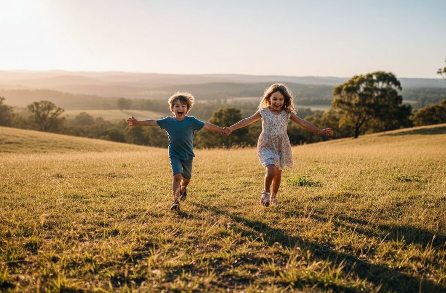 A heartwarming, professionally colour-graded photograph capturing joyful Eureka Victoria family adventure photography, showing two children laughing as they run through a sunlit, grassy field near the Eureka Stockade Memorial Park, with parents watching from a distance, evoking a sense of freedom and connection.