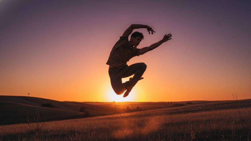A male dancer in mid-air, striking a powerful pose against a dramatic sunset over rolling hills in Exford, Victoria, for an Exford dance photography outdoor portraiture session. Professional photography, dramatic lighting, rich colours.