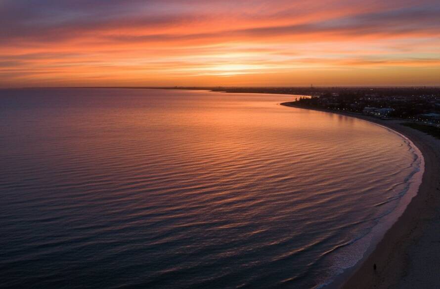 An epic moment captured by expert drone photography in Chelsea Heights, showing a stunning aerial perspective of a coastal sunset over the suburb, with vibrant colours reflecting on the calm water, highlighting a picturesque landscape.
