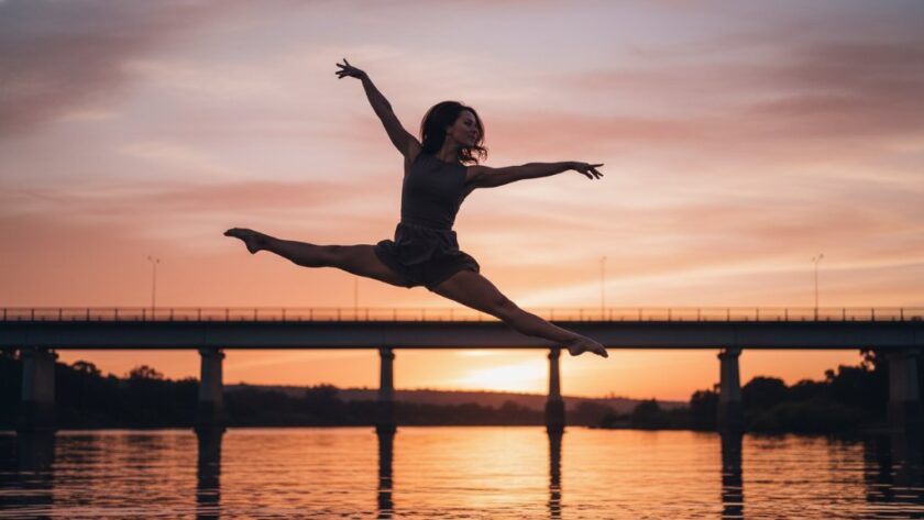 An epic moment of a contemporary dancer captured with expressive dance photography Orbost Victoria, performing a powerful leap against a soft-focused backdrop of the Orbost Bridge at sunset, showcasing incredible athleticism and artistry with dramatic lighting and professional colour grading.
