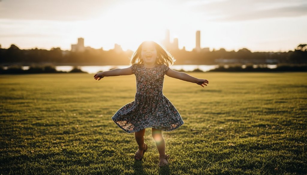 A joyful child, around 5 years old, running barefoot through an open grassy field in Footscray, Victoria, during golden hour. The child is holding a brightly coloured kite that soars against the clear blue sky. Dramatic backlight creates a beautiful halo effect around their hair, casting long shadows. The setting includes distant, blurred Footscray cityscape elements and the Maribyrnong River. Professional, cinematic photography with warm, vibrant colour grading and shallow depth of field, capturing an epic moment of freedom and happiness. This image represents Footscray vibrant kids photography sessions.
