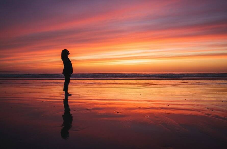 An awe-inspiring wide-angle shot of a lone figure silhouetted against a dramatic Frankston sunset, capturing the essence of Frankston's coastal fine art photography for stunning visuals, with vibrant orange and purple hues reflecting on the wet sand and gentle waves.