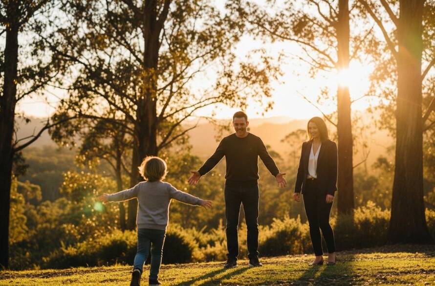 A heartwarming, genuine candid photography Upper Ferntree Gully families moment: A young child joyfully embracing their parent amidst the lush greenery of the Dandenong Ranges, sun flare creating a magical glow, captured with natural emotion.