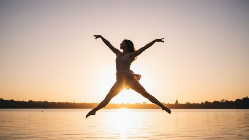 A breathtaking, professional photograph capturing a dancer in an elegant leap during a graceful dance photography Wendouree Lake sunset session, with golden hour light reflecting off the water and rich, cinematic colour grading.