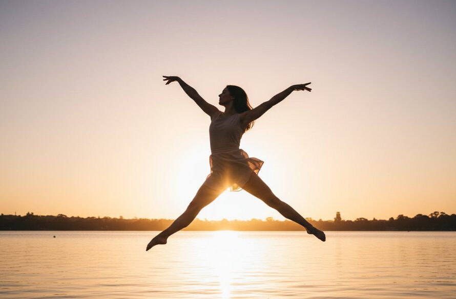 A breathtaking, professional photograph capturing a dancer in an elegant leap during a graceful dance photography Wendouree Lake sunset session, with golden hour light reflecting off the water and rich, cinematic colour grading.