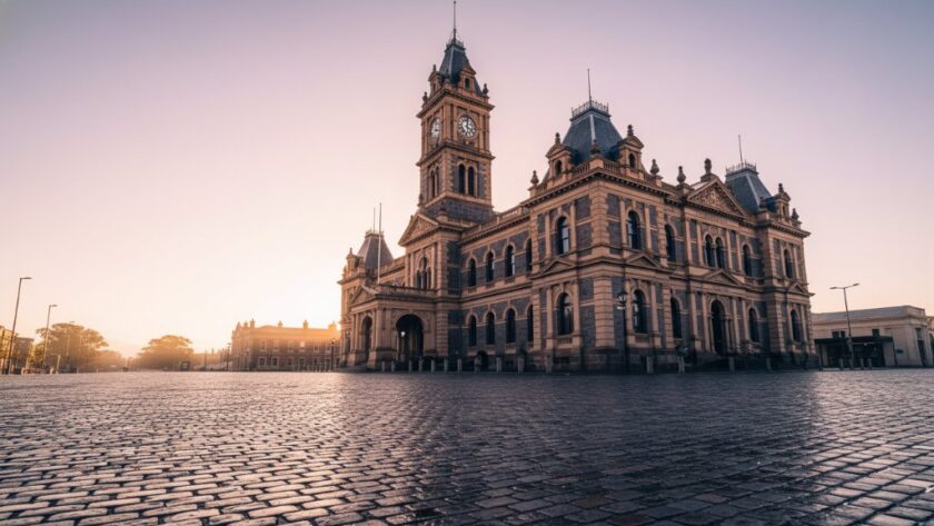 An epic, dramatic wide-angle shot of the historic Hamilton Botanic Gardens Gate Lodge at dawn, bathed in golden hour light, showcasing intricate Victorian-era details for a Hamilton Victoria heritage architecture photography portfolio.
