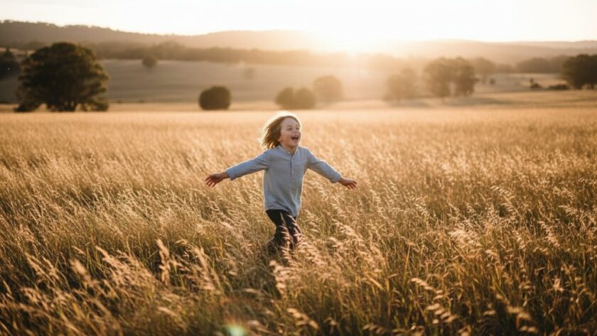 A wide-angle, cinematic photograph of a child, mid-laugh, running through a sun-drenched field in Heathcote, Victoria, with golden light flaring. This Heathcote Kids Outdoor Photography capturing genuine joy moment captures pure happiness and movement, showcasing the child's vibrant energy against the natural backdrop.
