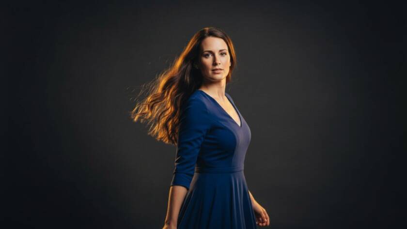 Heatherdale professional studio portrait photography of a confident young woman, bathed in dramatic golden light, standing strong against a dark background, showcasing power and grace.