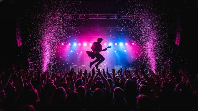 A dynamic wide shot showcasing Heathmont authentic live music photography Victoria, capturing a lead guitarist mid-shred under dramatic stage lights, with a cheering crowd silhouetted in the foreground and confetti falling, conveying raw energy and an epic concert moment.