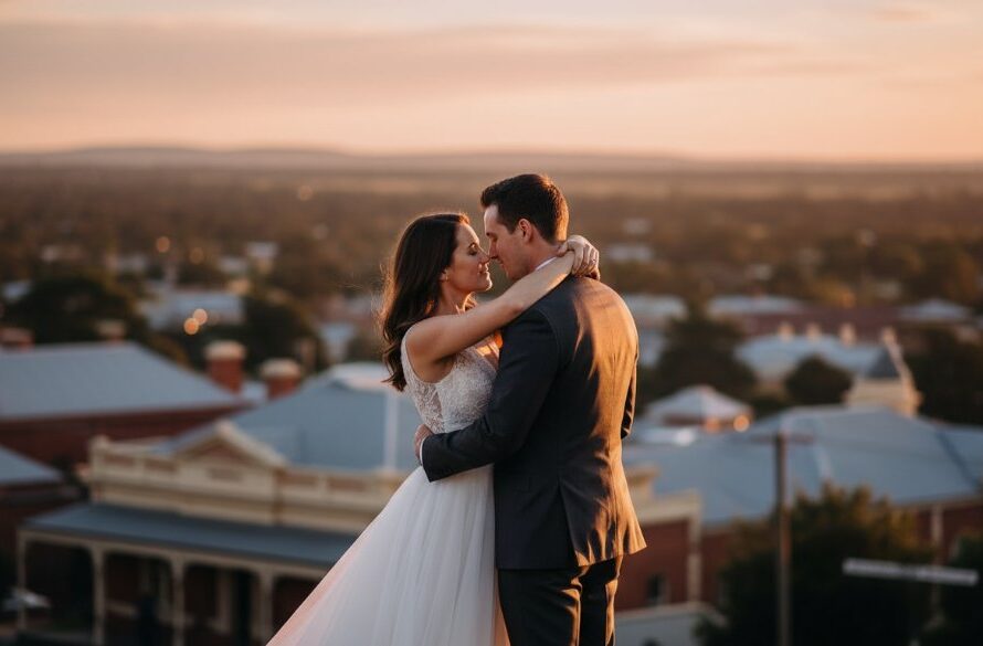 An epic moment captured in Intimate Maryborough Victoria Wedding Photography, showing a newly married couple sharing a tender kiss under the dramatic golden light of a setting sun, with the historic Maryborough Post Office facade blurred beautifully in the background. The scene is professionally colour-graded with a warm, romantic glow.