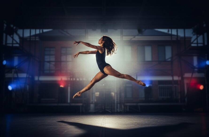 A female dancer in mid-air, caught in an incredible leap with powerful motion blur, backlighting from a stage light creating a halo effect, during a Keilor East dynamic dance performance photography session. The shot emphasizes grace and power against a darkened, atmospheric background.