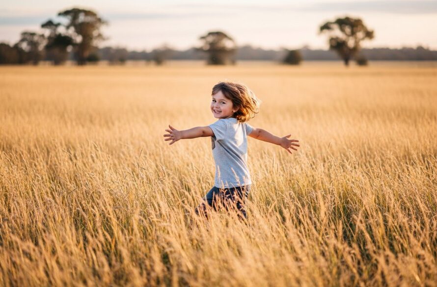 A joyful child, expertly captured by Kialla kids photography natural light specialists, laughing candidly in a golden field during sunset in Kialla, Victoria, with a sun-drenched, natural aesthetic.