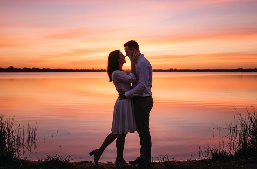 An epic, cinematic shot capturing a couple's joyous embrace by the water at sunset, showcasing stunning Kialla Lakes Engagement Photography Victoria, with dramatic golden hour lighting and reflection.