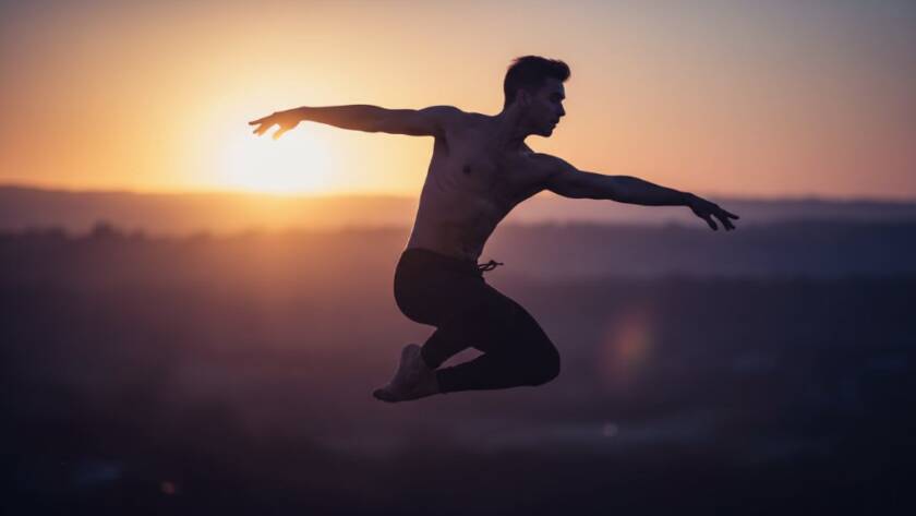 An epic moment captured through Knoxfield Dance Photography: Dynamic Movement Captured, showcasing a dancer in a powerful leap against a soft, dramatic backdrop, bathed in golden light, evoking grace and strength.
