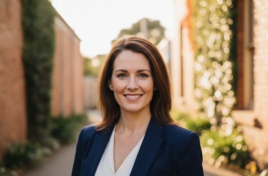 A professional woman, mid-laugh, looking directly at the camera with genuine warmth, captured outdoors in Korumburra at golden hour, showcasing Korumburra authentic professional headshots for local success. The background features blurred, rustic Korumburra architecture, emphasizing authenticity.
