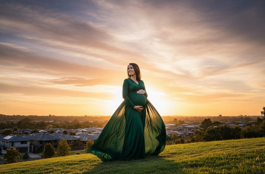 An elegant expectant mother, in a flowing amber gown, bathed in the soft glow of a golden hour sunset over a tranquil, modern park in Lucas, Victoria, depicting a Lucas Victoria elegant maternity photoshoot.