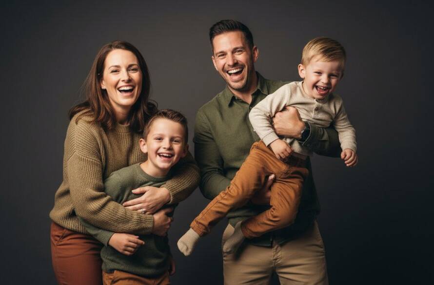 An emotionally resonant, wide-angle professional photograph capturing a joyous family of four mid-embrace in a sleek studio, with soft, dramatic rim lighting highlighting their faces and a backdrop of elegant, muted grey. This epic moment embodies Luxury Studio Family Photos Malvern East Victoria, showcasing deep connections and timeless joy.