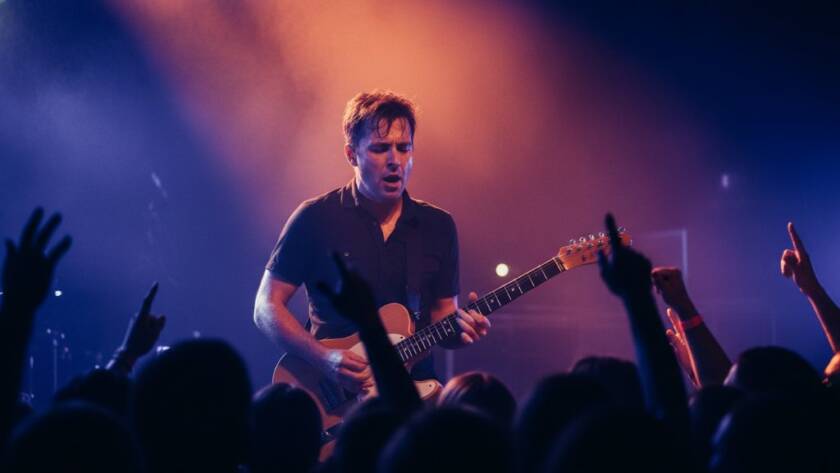 An epic moment of Malvern East concert photography storytelling, featuring a lead singer bathed in dramatic purple and blue stage lights, passionately performing to a cheering crowd at a local Malvern East venue in Victoria, with dynamic energy captured in stunning detail by a professional photographer.
