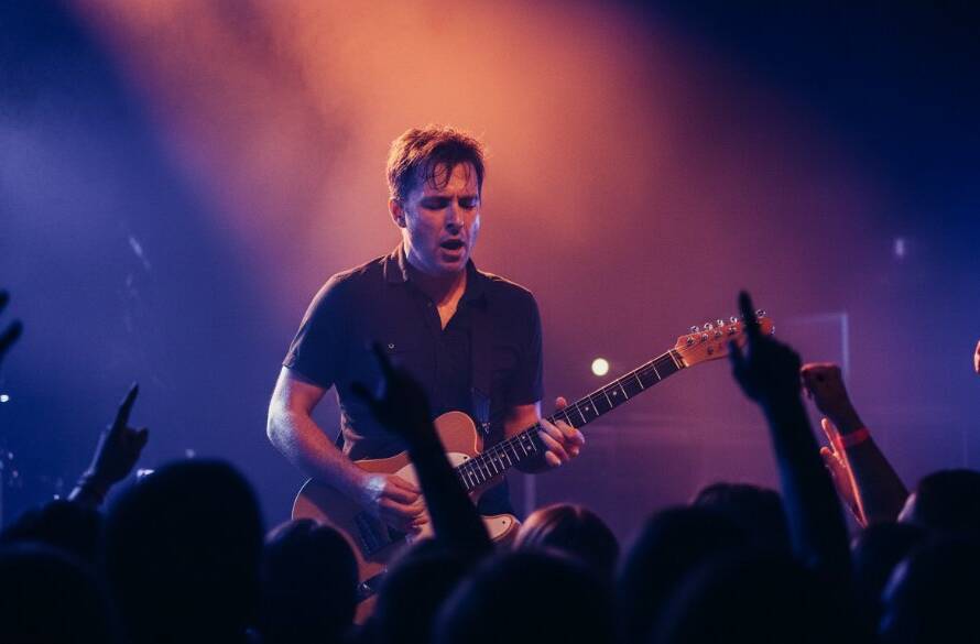 An epic moment of Malvern East concert photography storytelling, featuring a lead singer bathed in dramatic purple and blue stage lights, passionately performing to a cheering crowd at a local Malvern East venue in Victoria, with dynamic energy captured in stunning detail by a professional photographer.