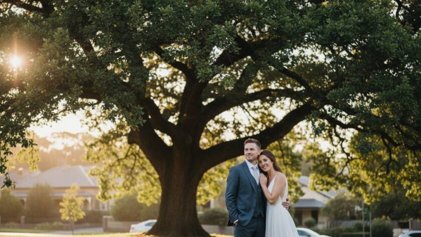A beautifully composed, candid photograph capturing a joyful newlywed couple sharing an intimate laugh during their Malvern East Wedding Photography Candid Moments, with soft, golden hour light filtering through mature oak trees in a Malvern East garden, showcasing genuine emotion and the picturesque local setting.