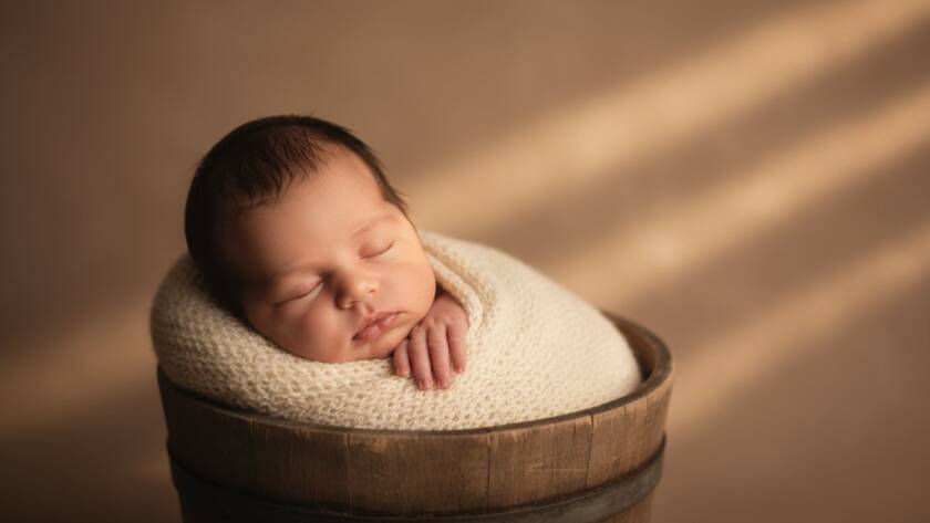 A close-up, warm-toned portrait from Manor Lakes newborn photography capturing tiny details, showing a sleeping baby's tiny hand gently grasping their parent's finger, bathed in soft, ethereal natural light, with shallow depth of field, evoking a sense of pure love and connection, set against a subtle, elegant backdrop.