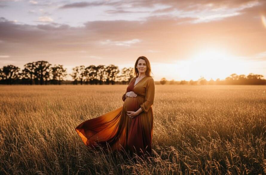 A radiant mother-to-be in an elegant gown, cradling her baby bump, captured during a professional Melton Victoria outdoor maternity photography session at sunset, with dramatic, warm lighting filtering through gum trees.