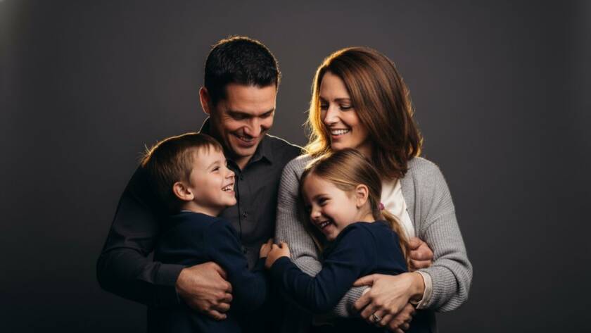A joyous Boronia family of four, parents embracing two laughing children, captured in a modern studio portrait photography Boronia families style, with dramatic lighting creating a warm, intimate atmosphere, showcasing genuine connection.