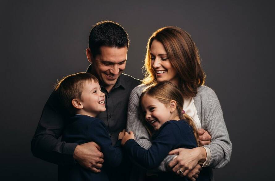 A joyous Boronia family of four, parents embracing two laughing children, captured in a modern studio portrait photography Boronia families style, with dramatic lighting creating a warm, intimate atmosphere, showcasing genuine connection.